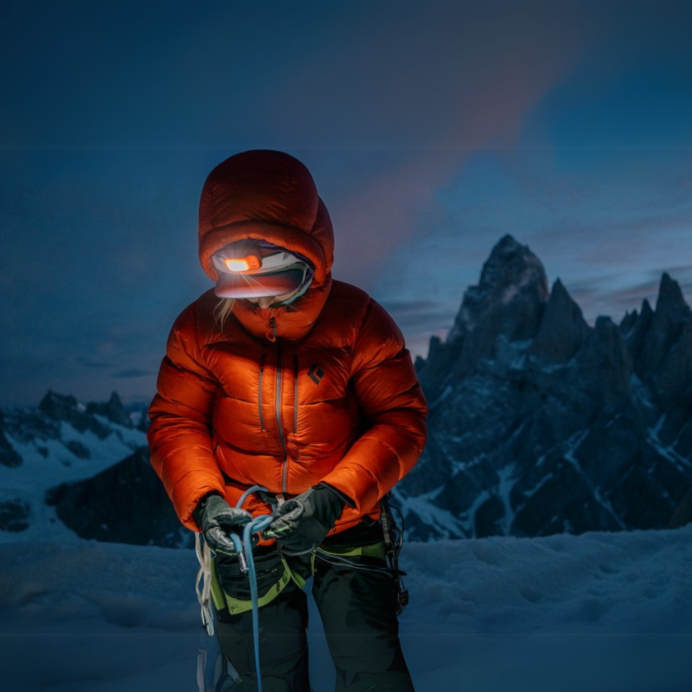 
Black Diamond led-hoofdlamp gebruikt door een klimmer in rode donsjas die een klimtouw vastmaakt in de sneeuw