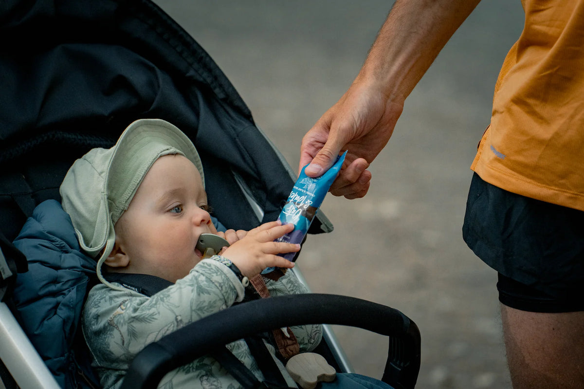 Moonvalley Oats and Dates Chocolate and Sea Salt energy bar wordt aangeboden aan een kind in een kinderwagen tijdens een wandeling