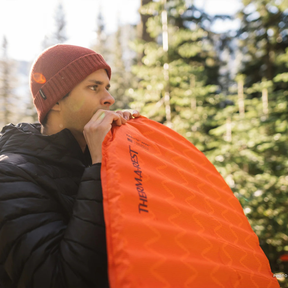  Persoon blaast de rode Therm-a-Rest ProLite Apex Heat Wave L slaapmat op in een bergachtige omgeving   
