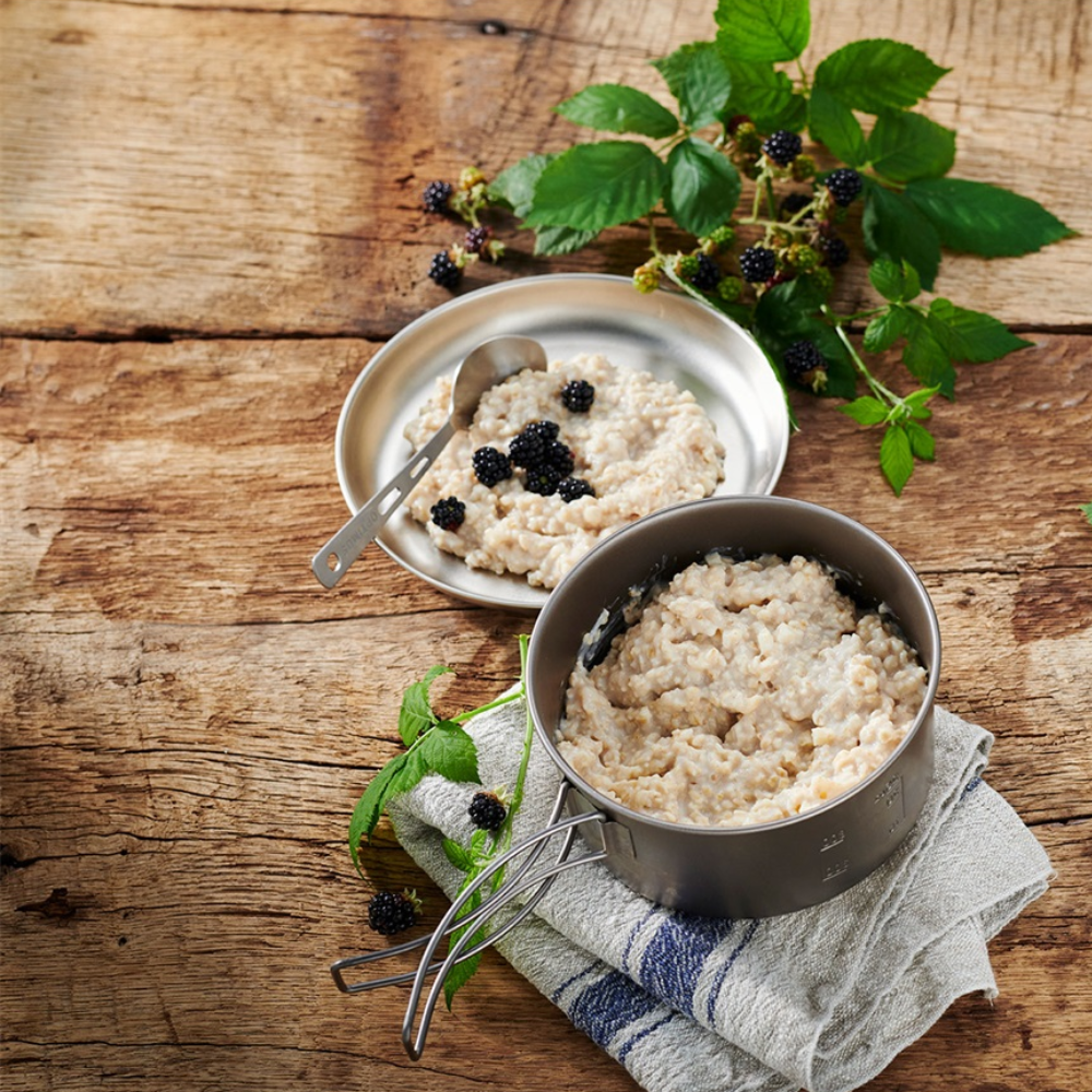 Trek'n Eat Breakfast Porridge Apple bereid in een pannetje op houten tafel met bessen en groen   