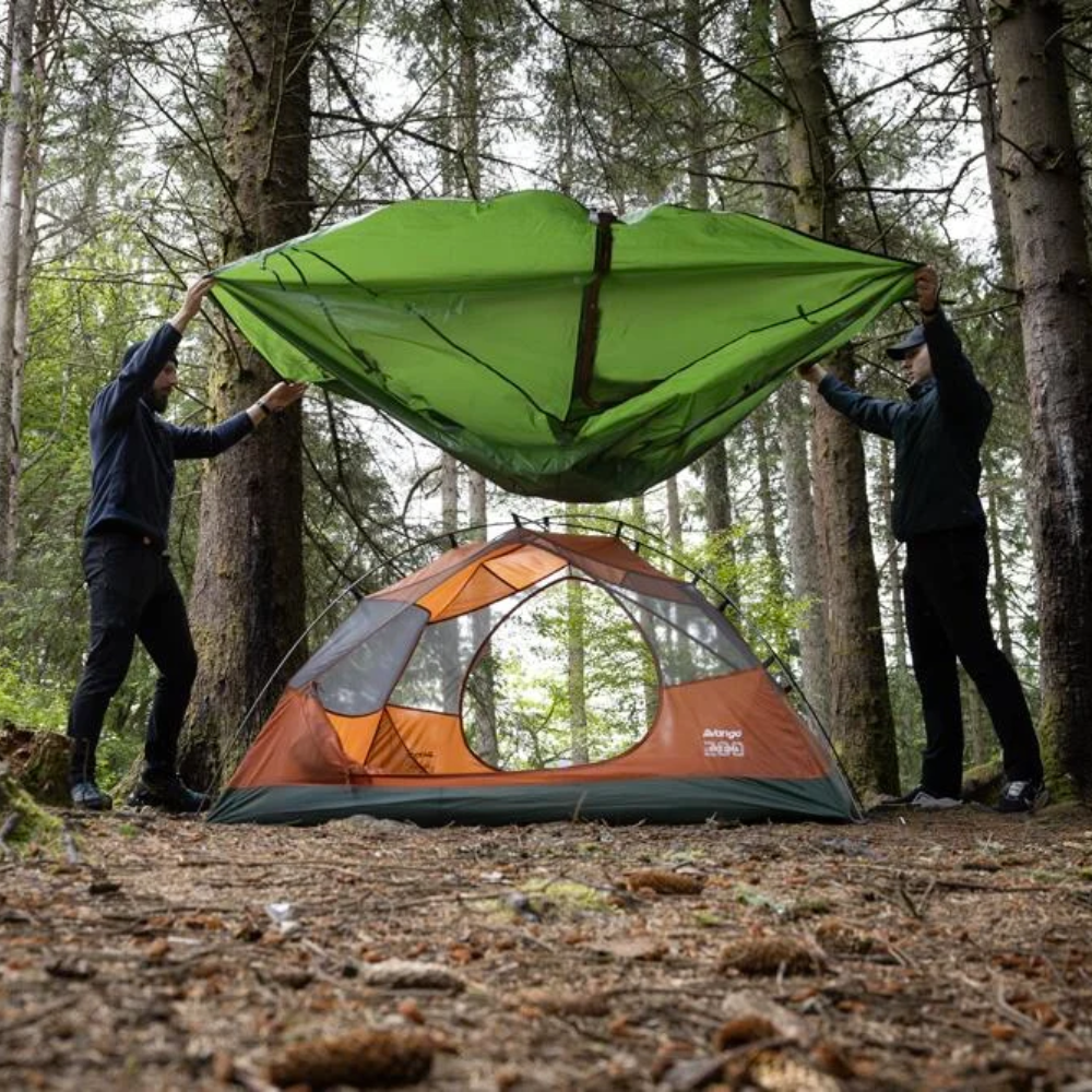 Twee personen die de buitentent van een Vango tent over de binnentent spannen in een bosrijke omgeving